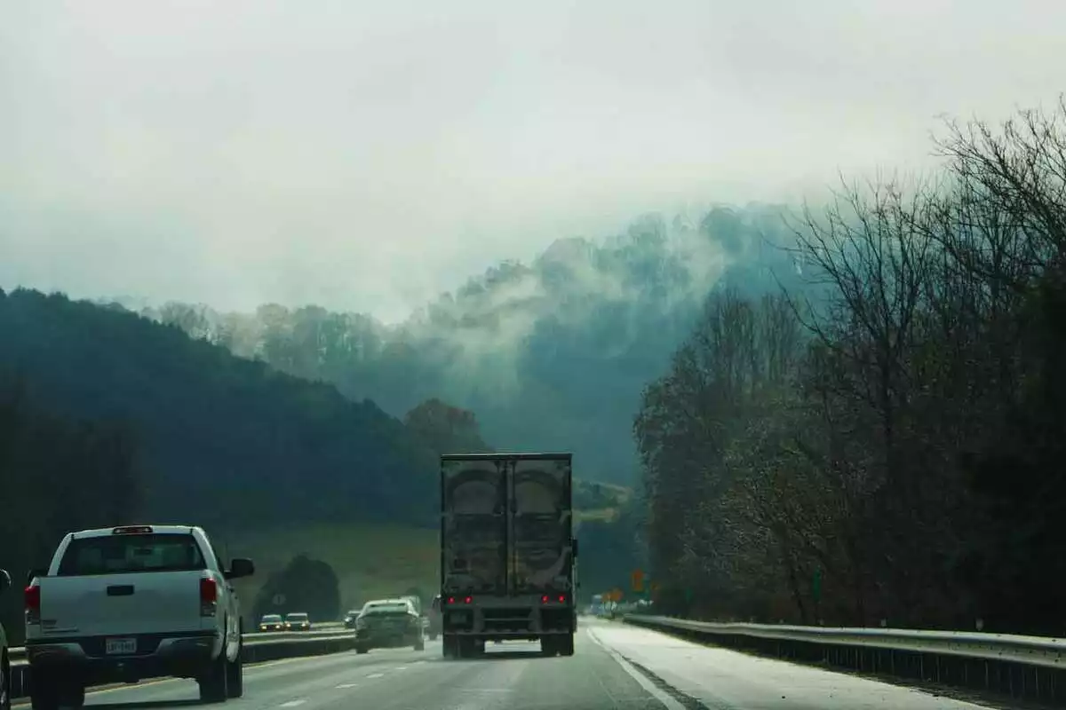 Coches y un camión circulando por una carretera con montañas de fondo