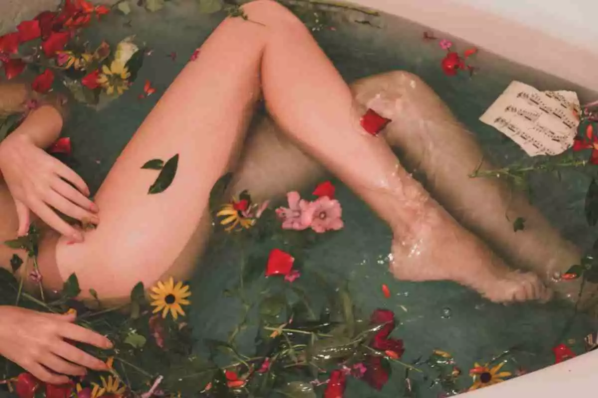 Fotografía de las piernas de una mujer en una bañera con flores