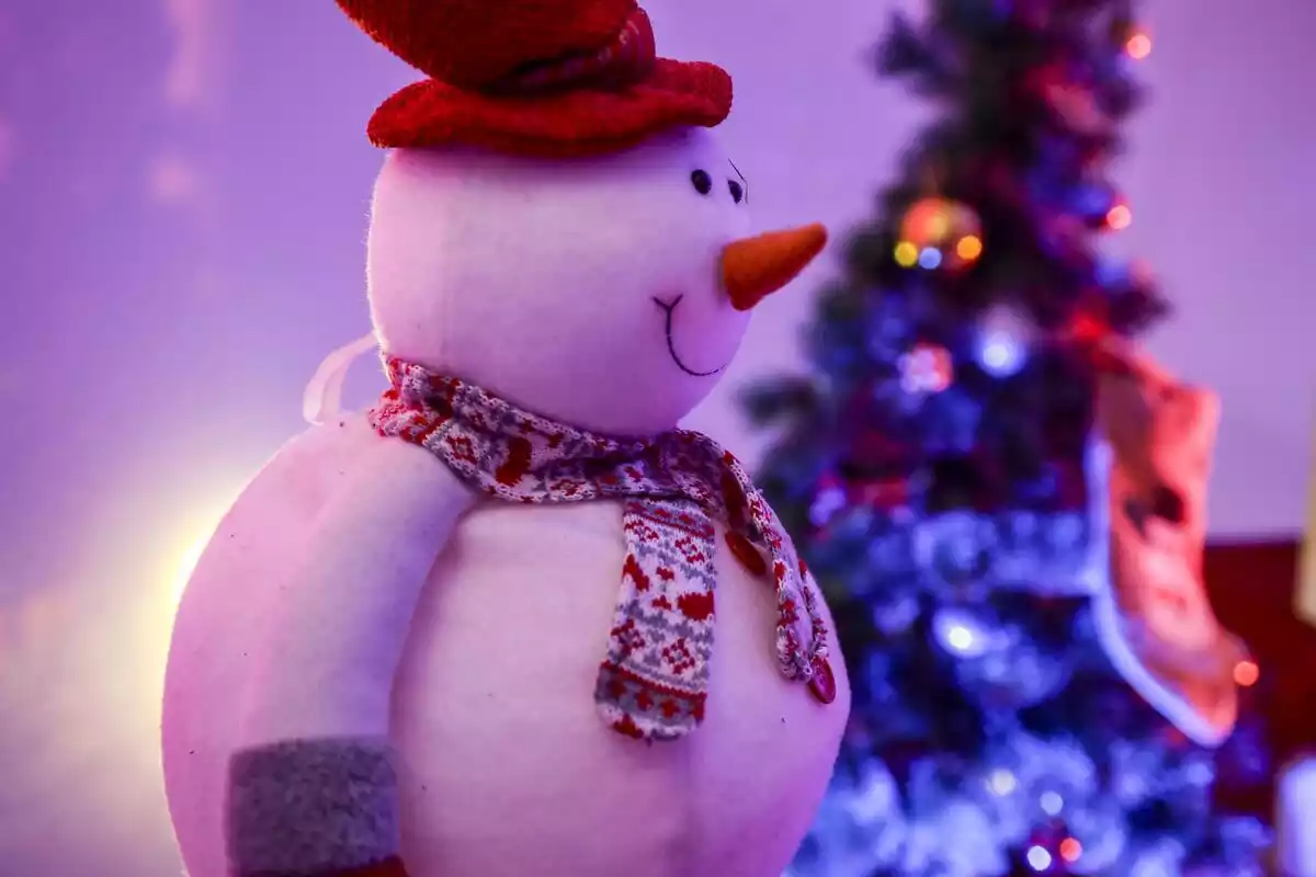 Peluche de un muñeco de nieve con un árbol de navidad de fondo