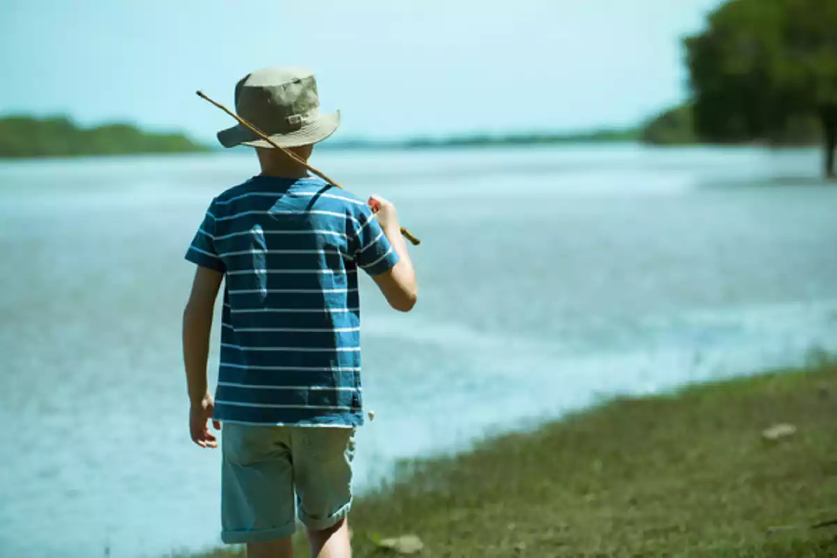 Niño con una caña de pescar paseando por el lado de un lago