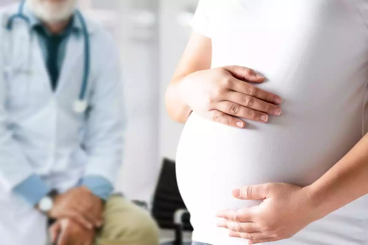 Una mujer embarazada se sujeta la barriga y su doctor la observa