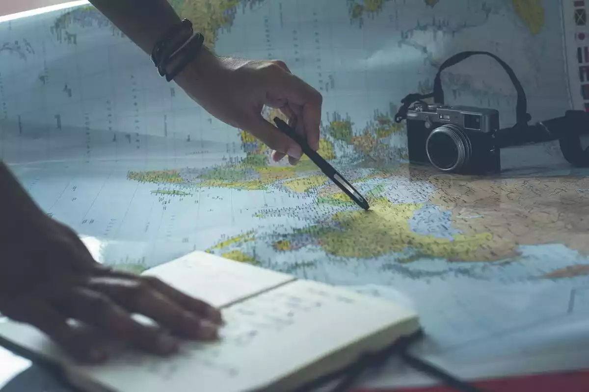 manos con libreta, mapa, bolígrafo y cámara preparando un viaje