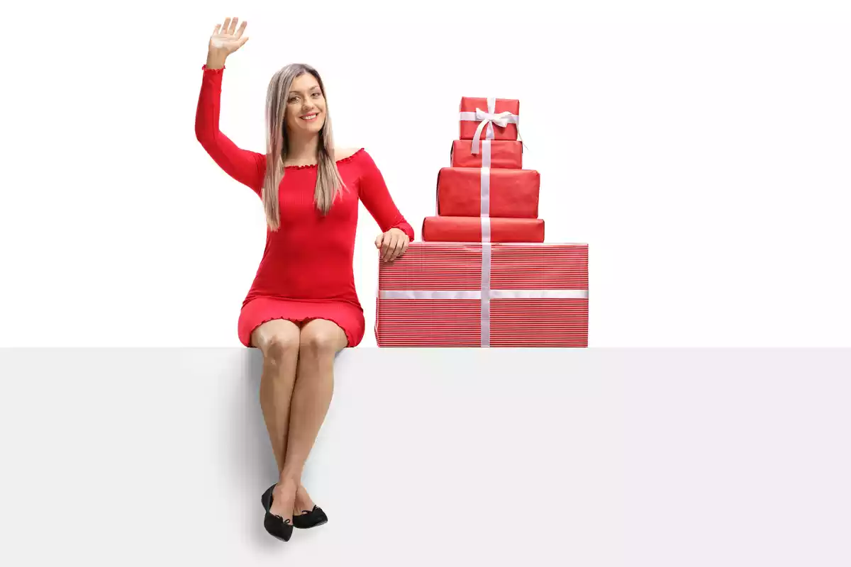 Chica con vestido rojo corto posando al lado de unos regalos de navidad