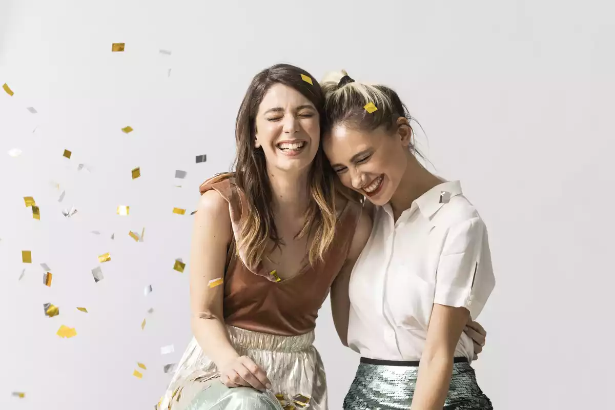 Dos amigas riéndose y rodeadas de confeti