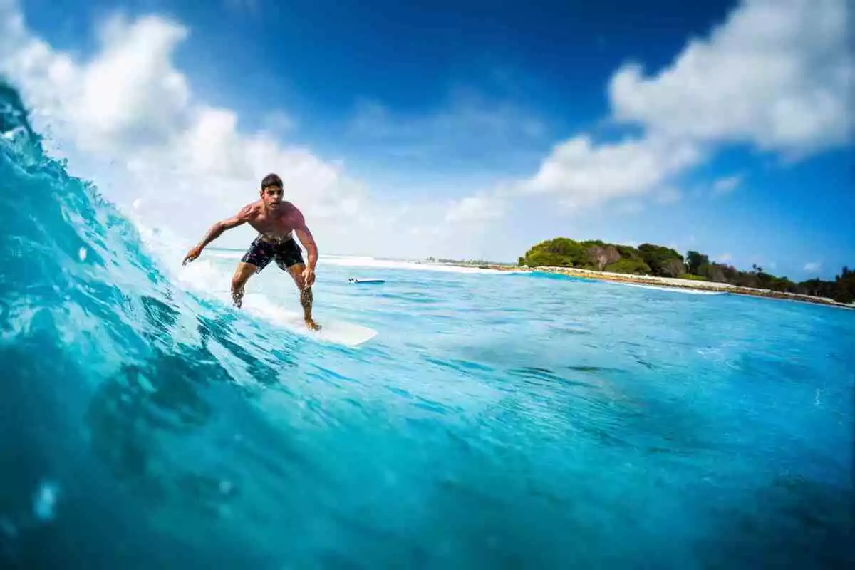 Joven surfista atlético monta la ola oceánica en el punto de surf Sultans en Maldivas