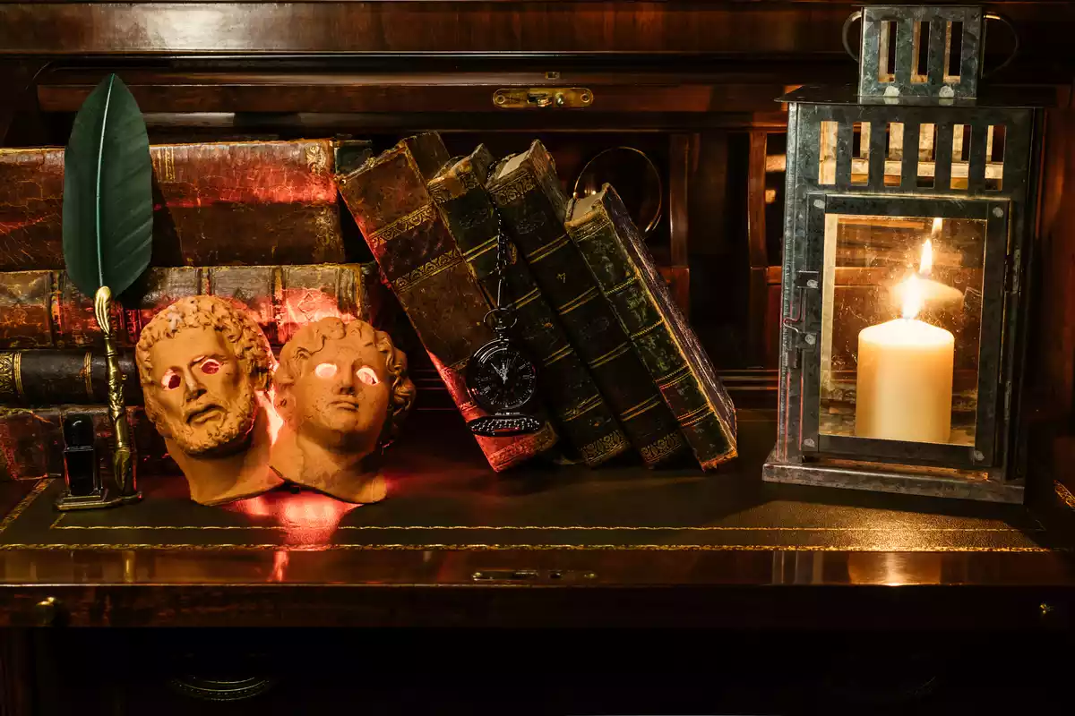 Libros en una estantería rodeados de una vela y máscaras