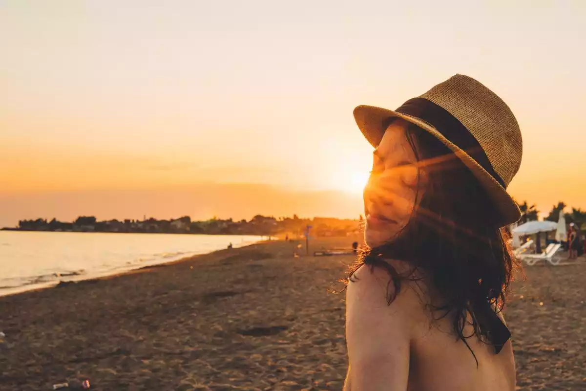 Puesta de sol en la playa con chica con sombrero en primer plano