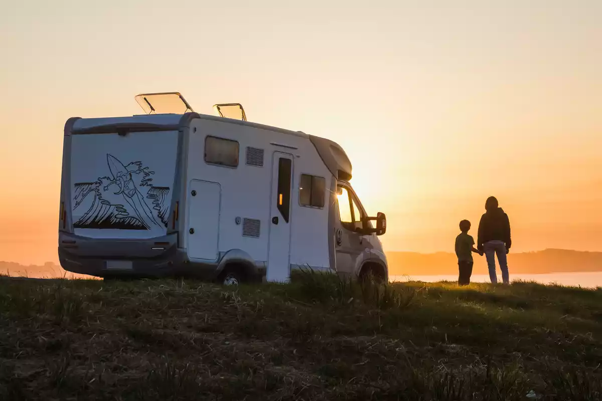 Una caravana y dos personas delante de una puesta de sol